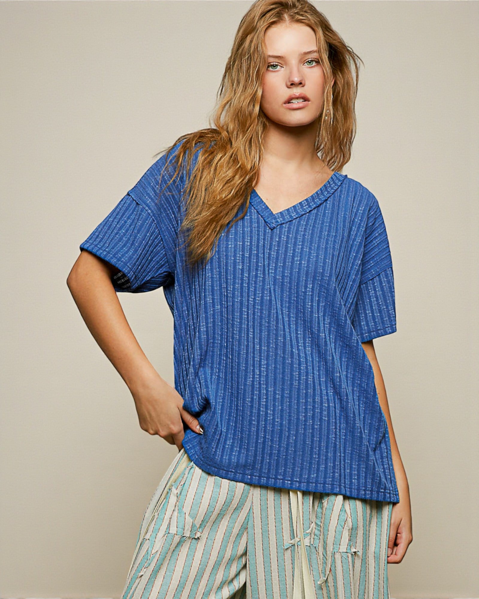 Woman wearing a blue textured top and striped pants against a beige background