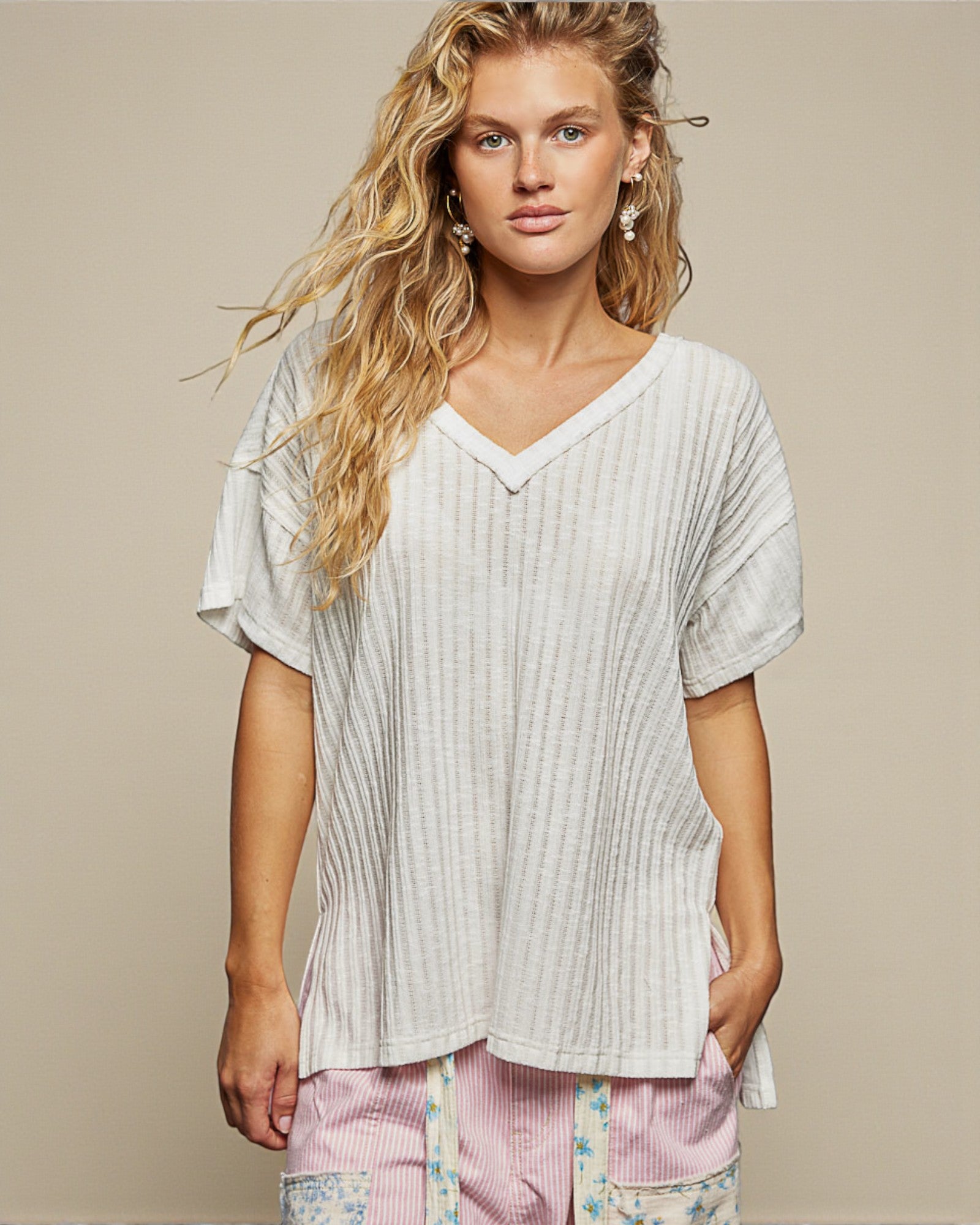 Woman wearing a white textured top with floral pants on a beige background