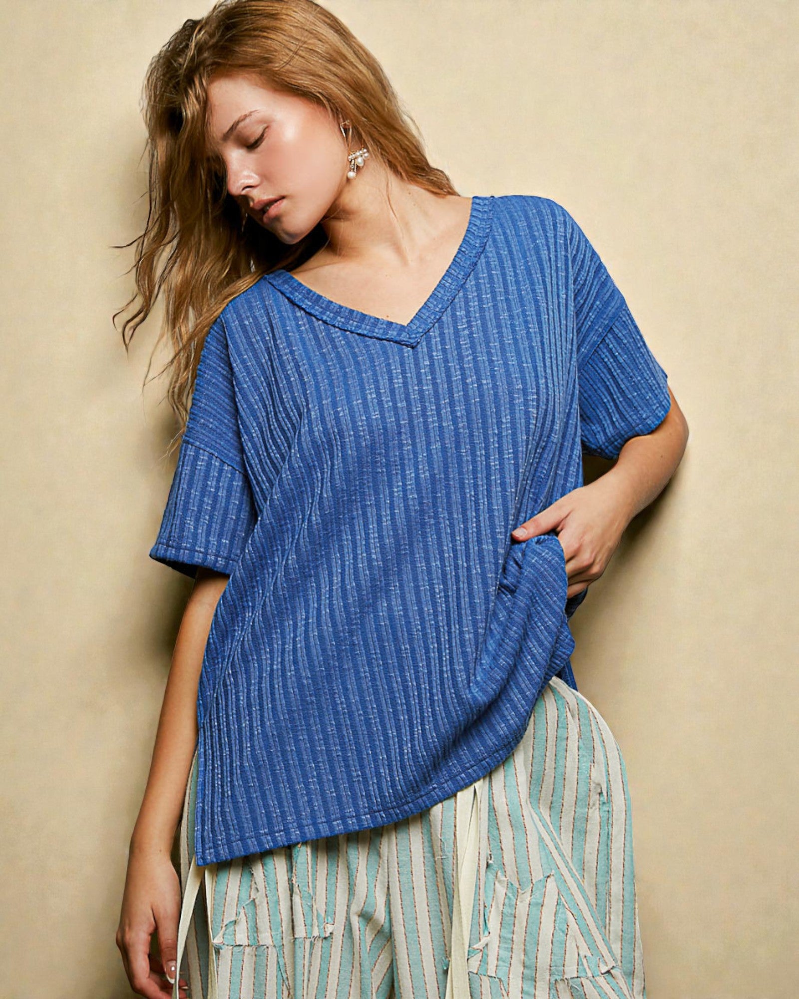 Woman wearing a blue textured top and striped pants against a beige background