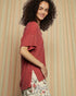 Woman wearing a red textured top with a floral skirt against a beige curtain background