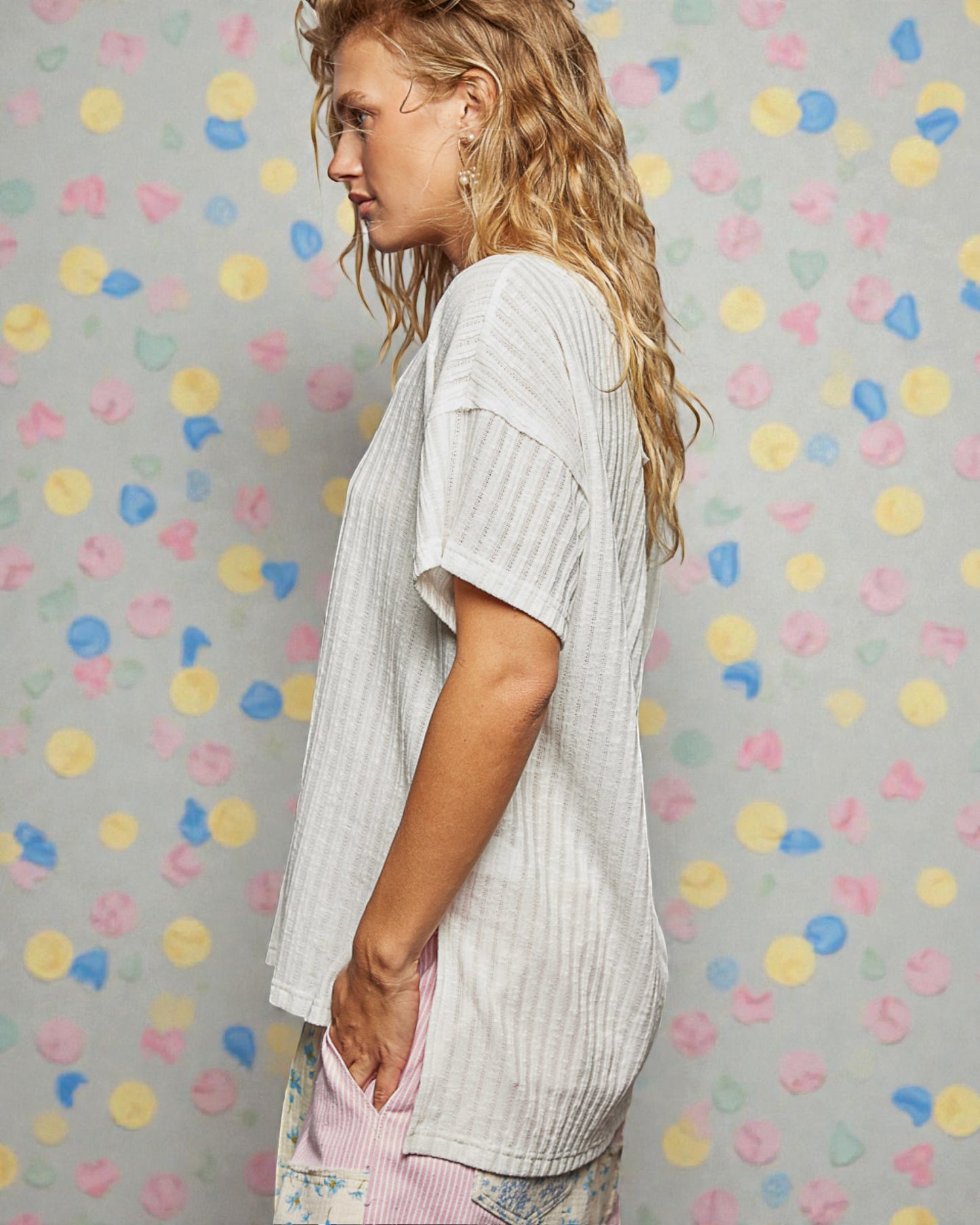 Woman wearing a light-colored top and patterned pants against a polka dot wall.