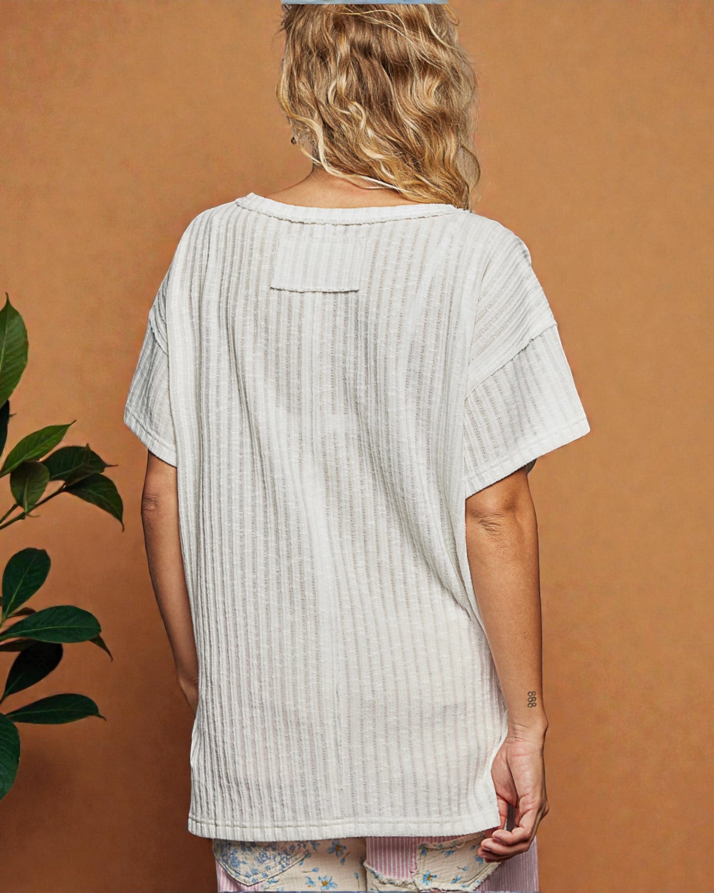 Person wearing a light-colored ribbed top against a brown background