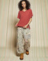 Woman wearing a red top and patterned pants against a neutral background