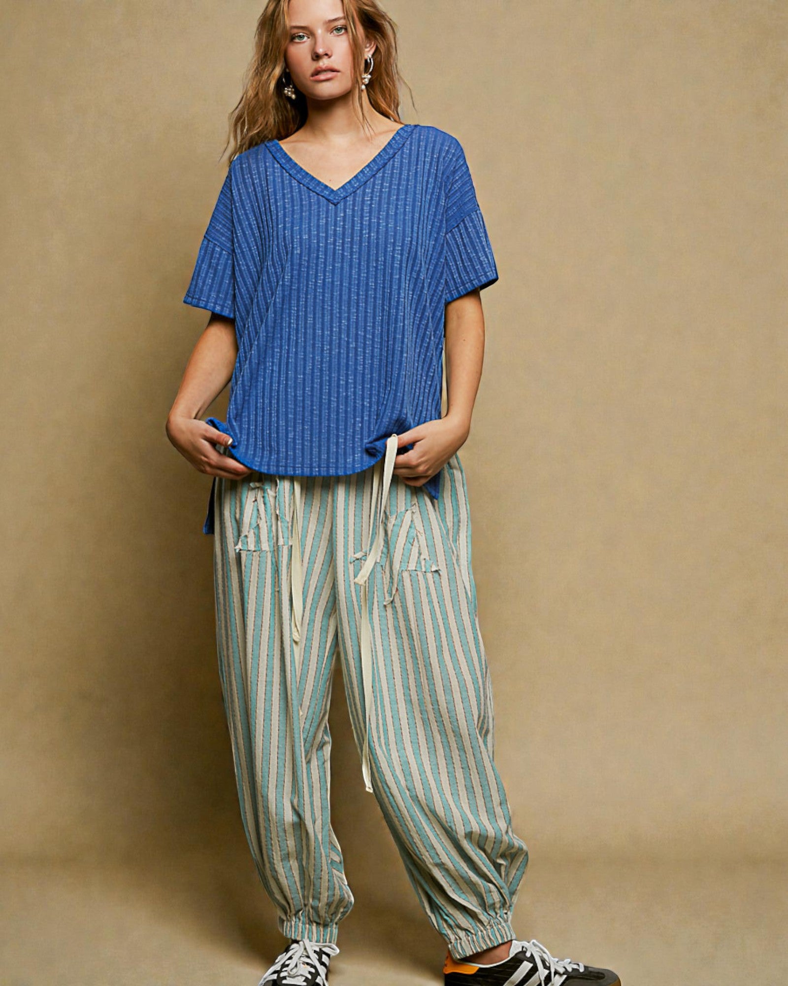 Woman wearing a blue oversized shirt and striped pants against a beige background