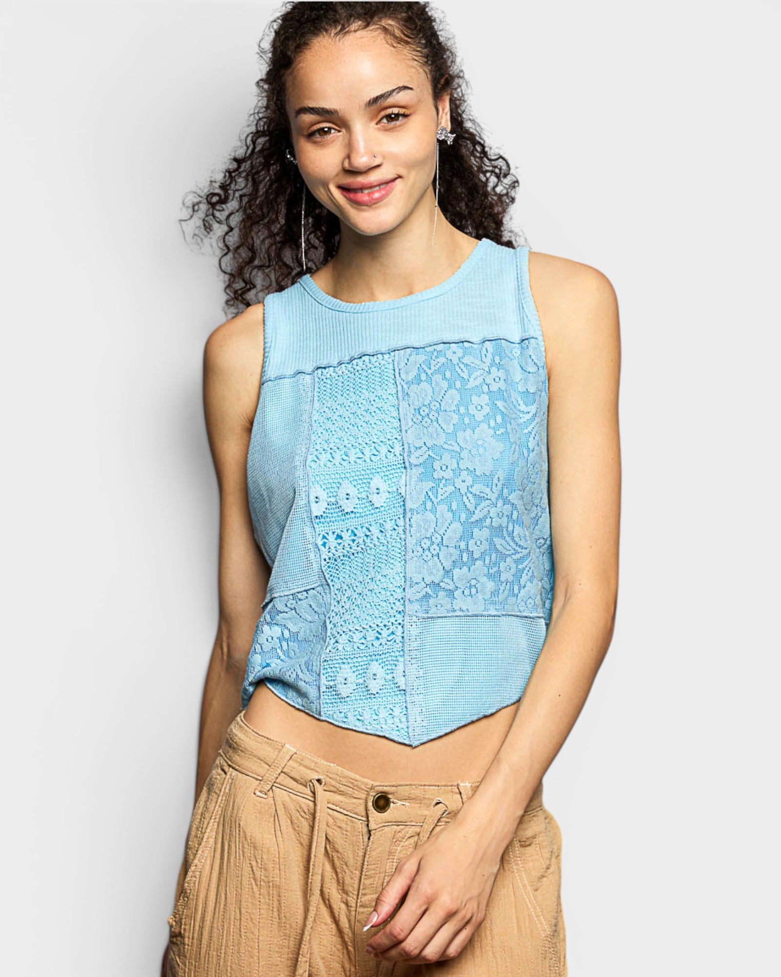 Woman wearing a light blue sleeveless top with lace details on a plain background