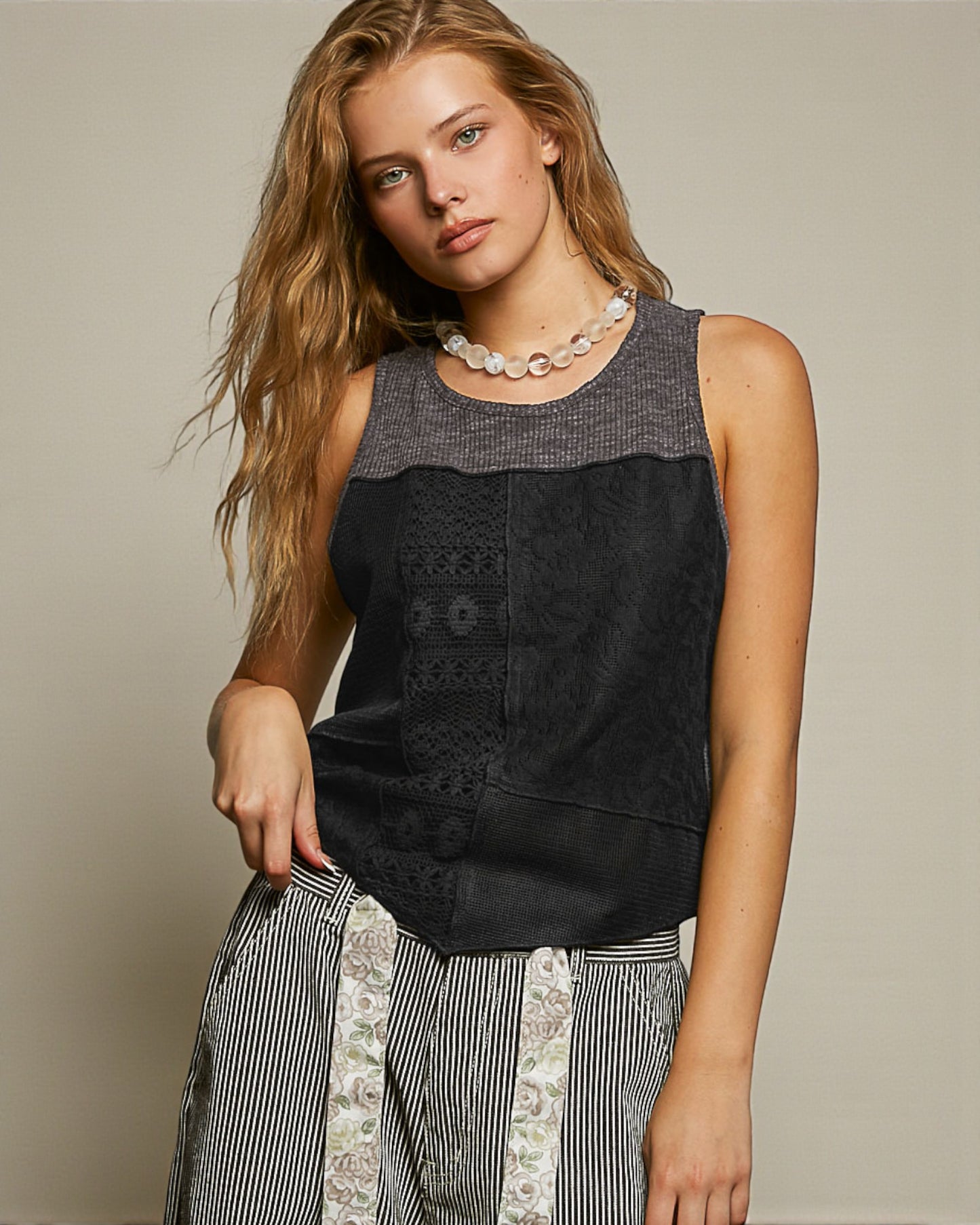 Woman wearing a black sleeveless top with patterned trim against a neutral background