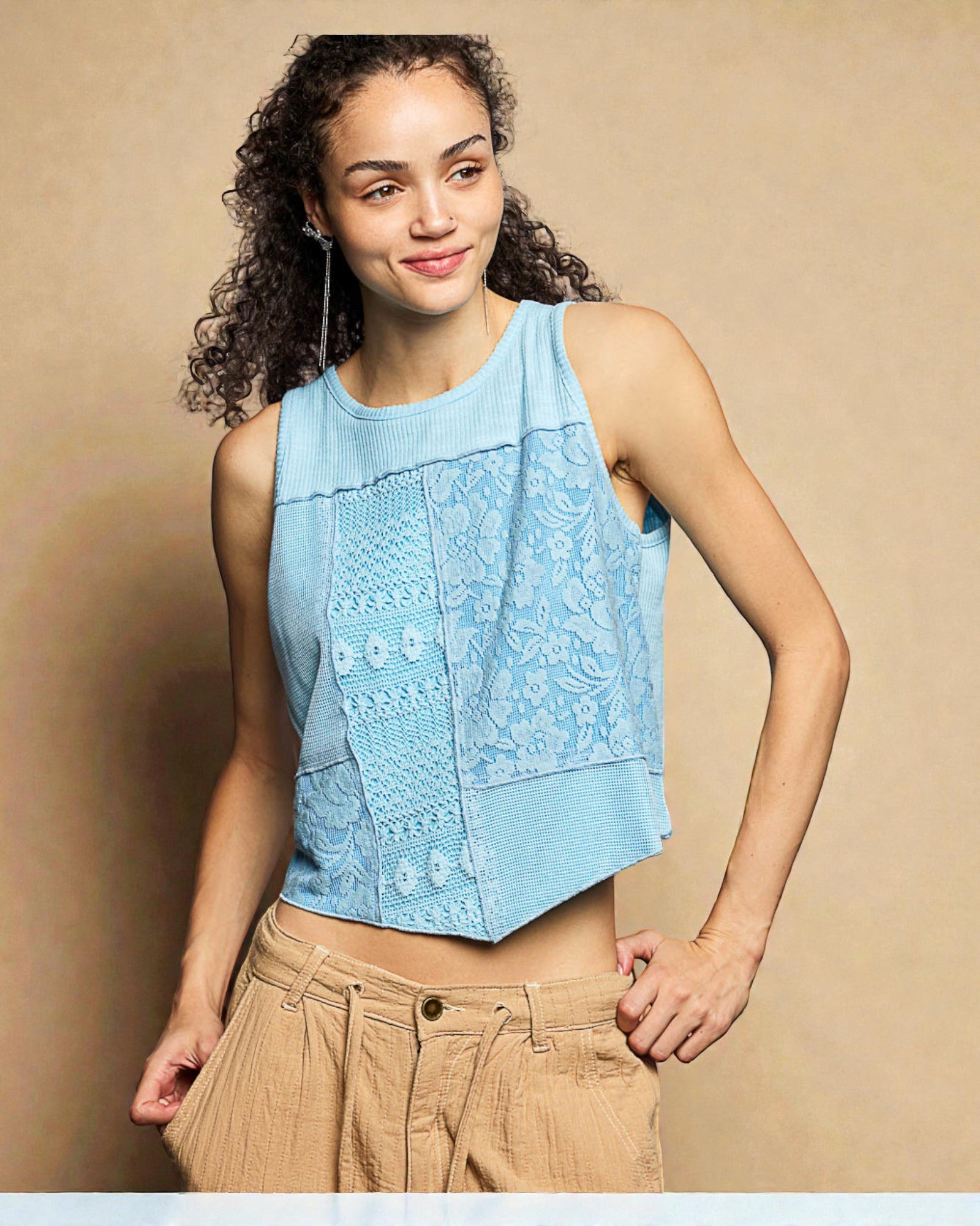 Woman wearing a light blue sleeveless top with lace details against a beige background