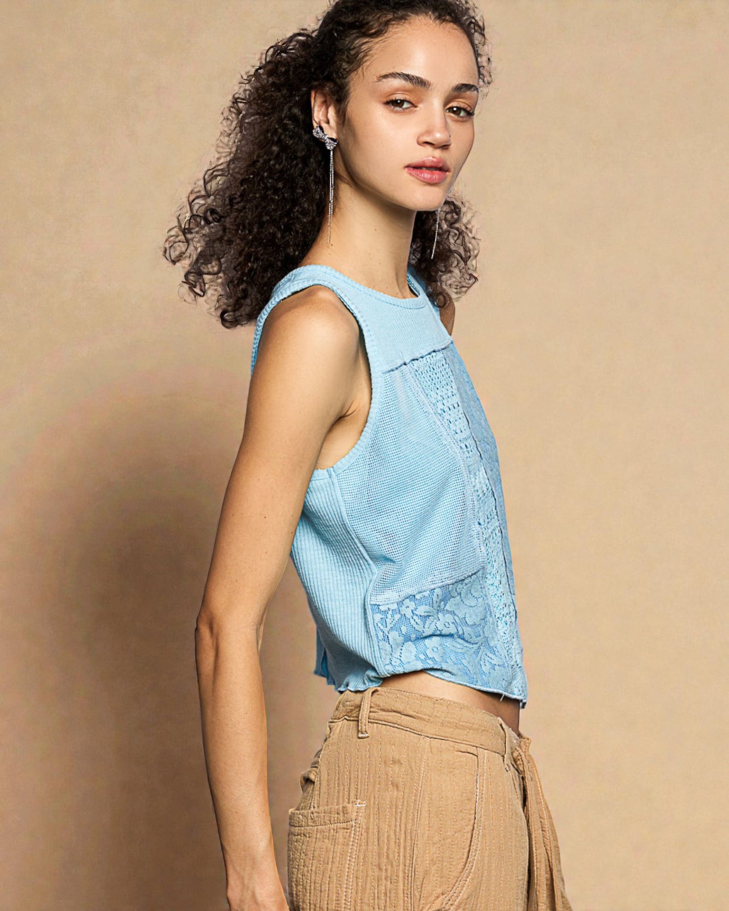 Woman wearing a light blue sleeveless top and beige pants against a beige background