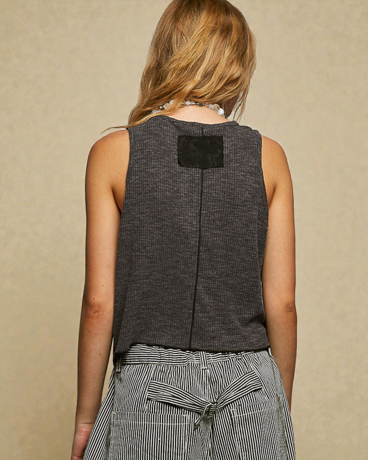 Person wearing a sleeveless dark gray top with a beige background