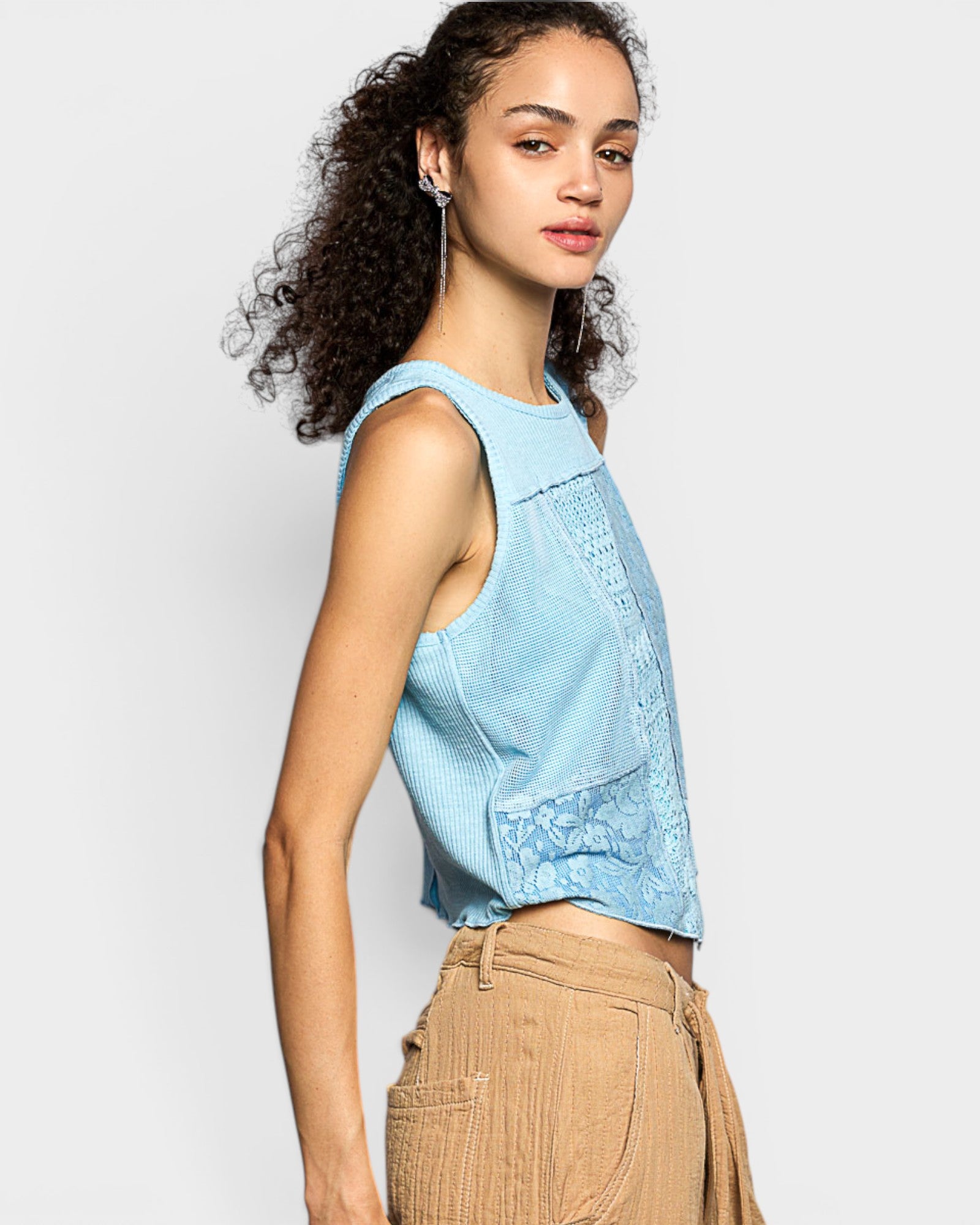 Woman wearing a light blue sleeveless top and beige pants on a white background