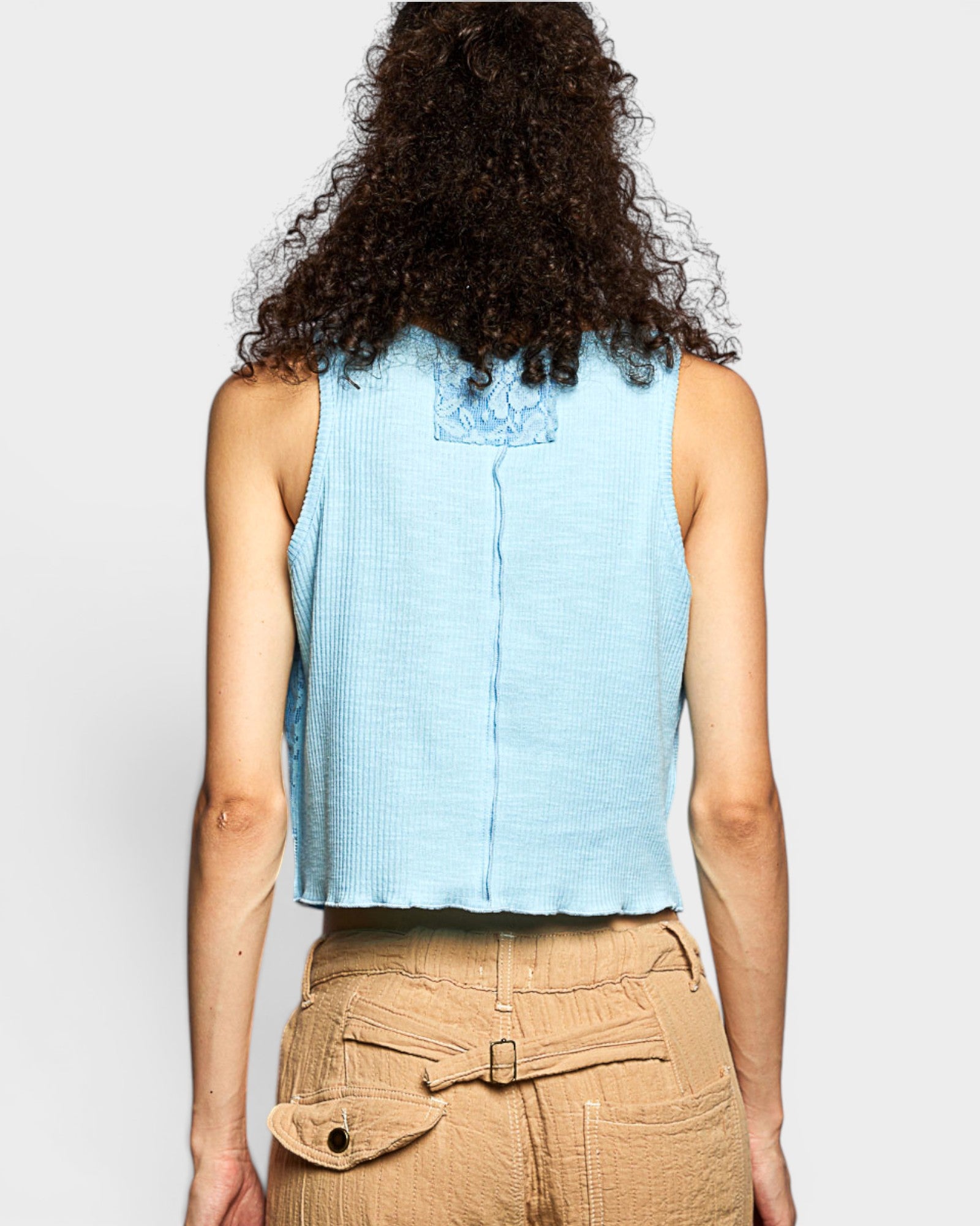Person wearing a light blue sleeveless top and beige pants on a white background
