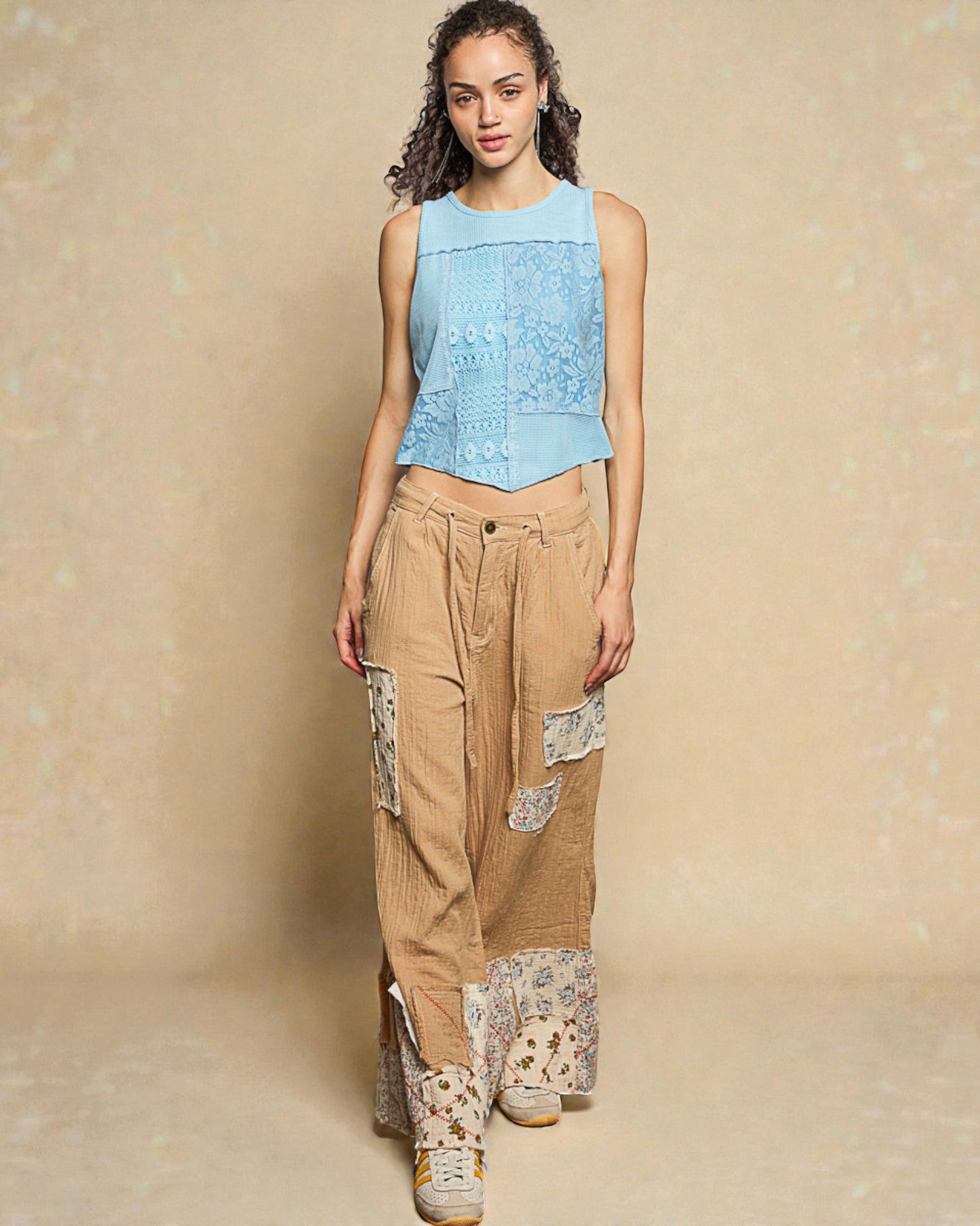 Woman wearing a light blue sleeveless top and beige pants with floral patterns on a beige background