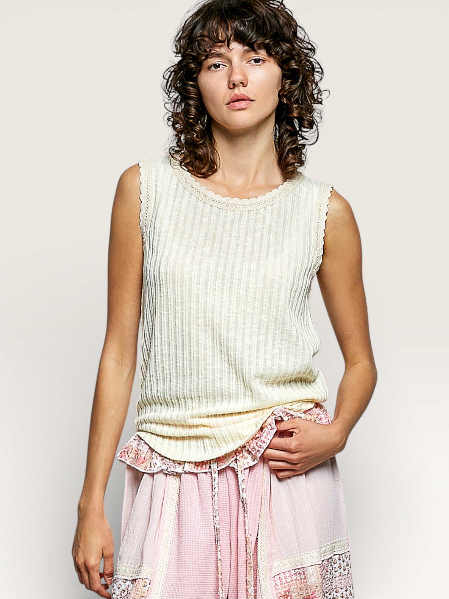 Woman wearing a sleeveless ribbed top and pink skirt with lace details on a plain background