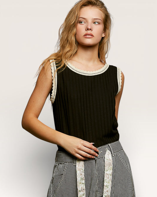 Woman wearing a black sleeveless top with lace details on a plain background