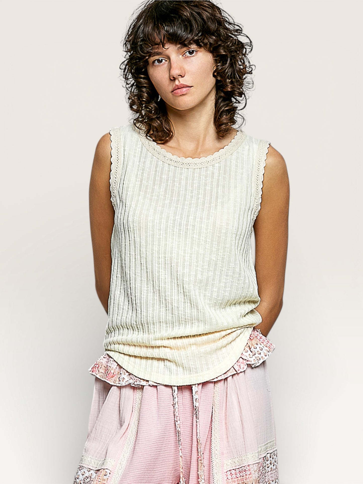 Woman wearing a light-colored sleeveless top with pink pants against a plain background