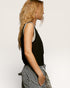 Woman wearing a black sleeveless top with white trim on a plain background