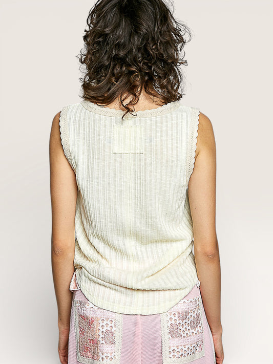 Person wearing a light-colored sleeveless top with a plain background