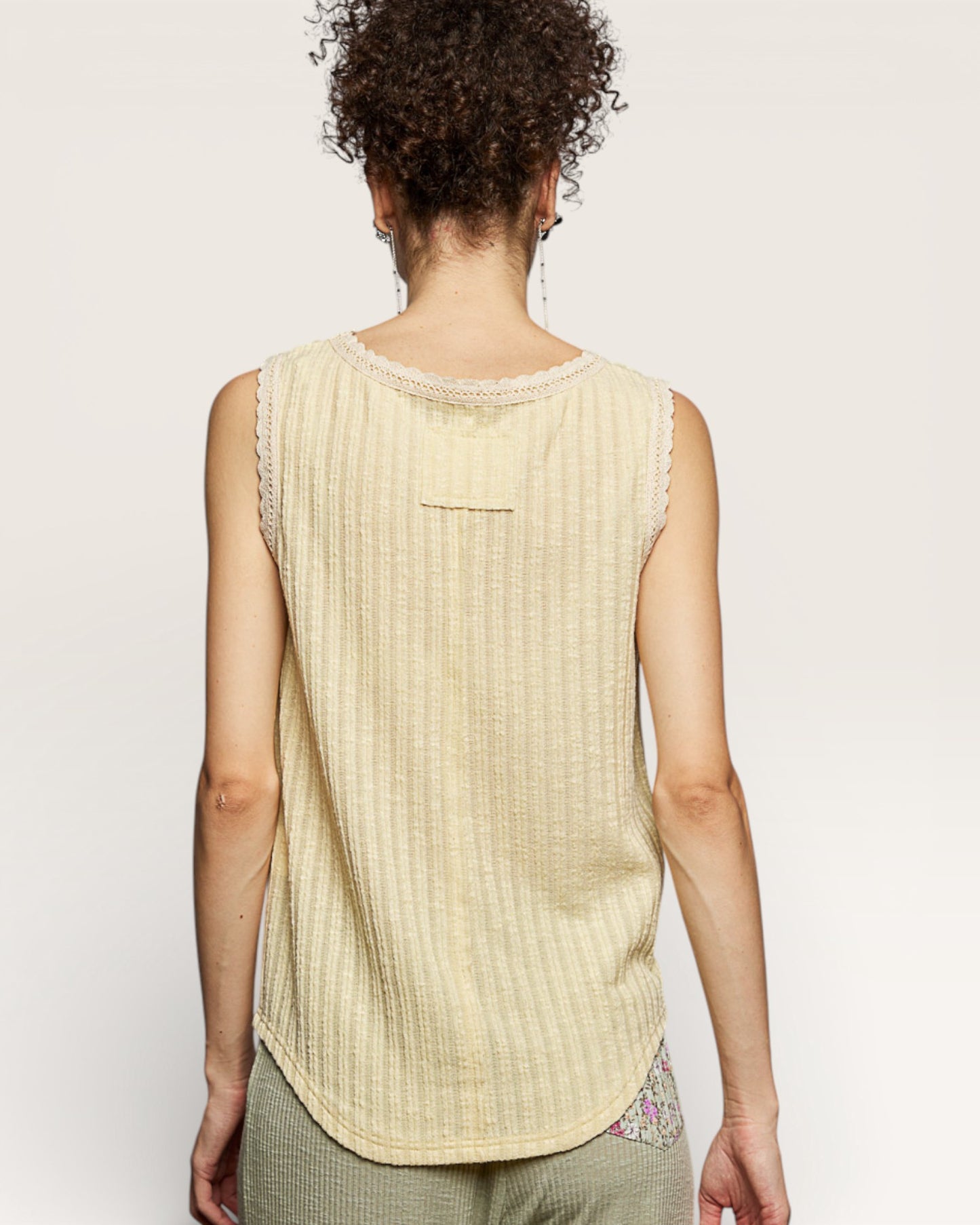 Person wearing a beige sleeveless top with lace trim on a plain background
