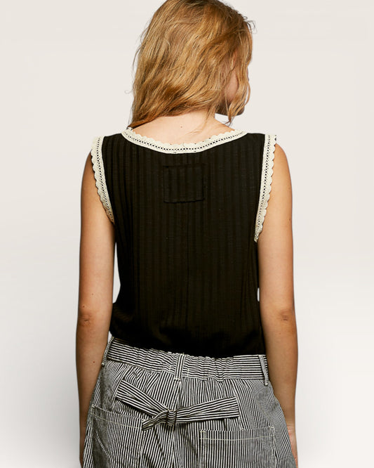 Woman wearing a black sleeveless top with white trim on a plain background