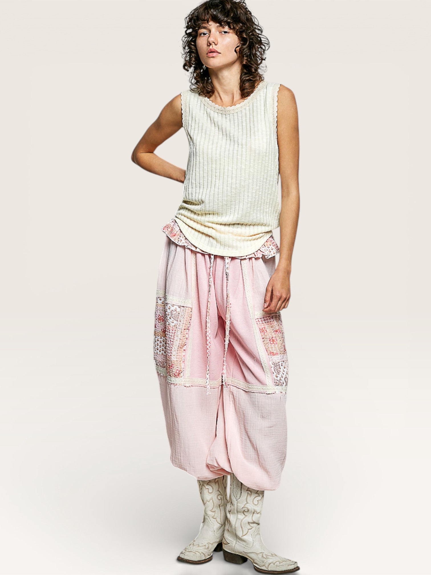 Woman wearing a light green sleeveless top and pink pants with floral patterns on a white background