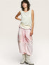 Woman wearing a light green sleeveless top and pink pants with floral patterns on a white background