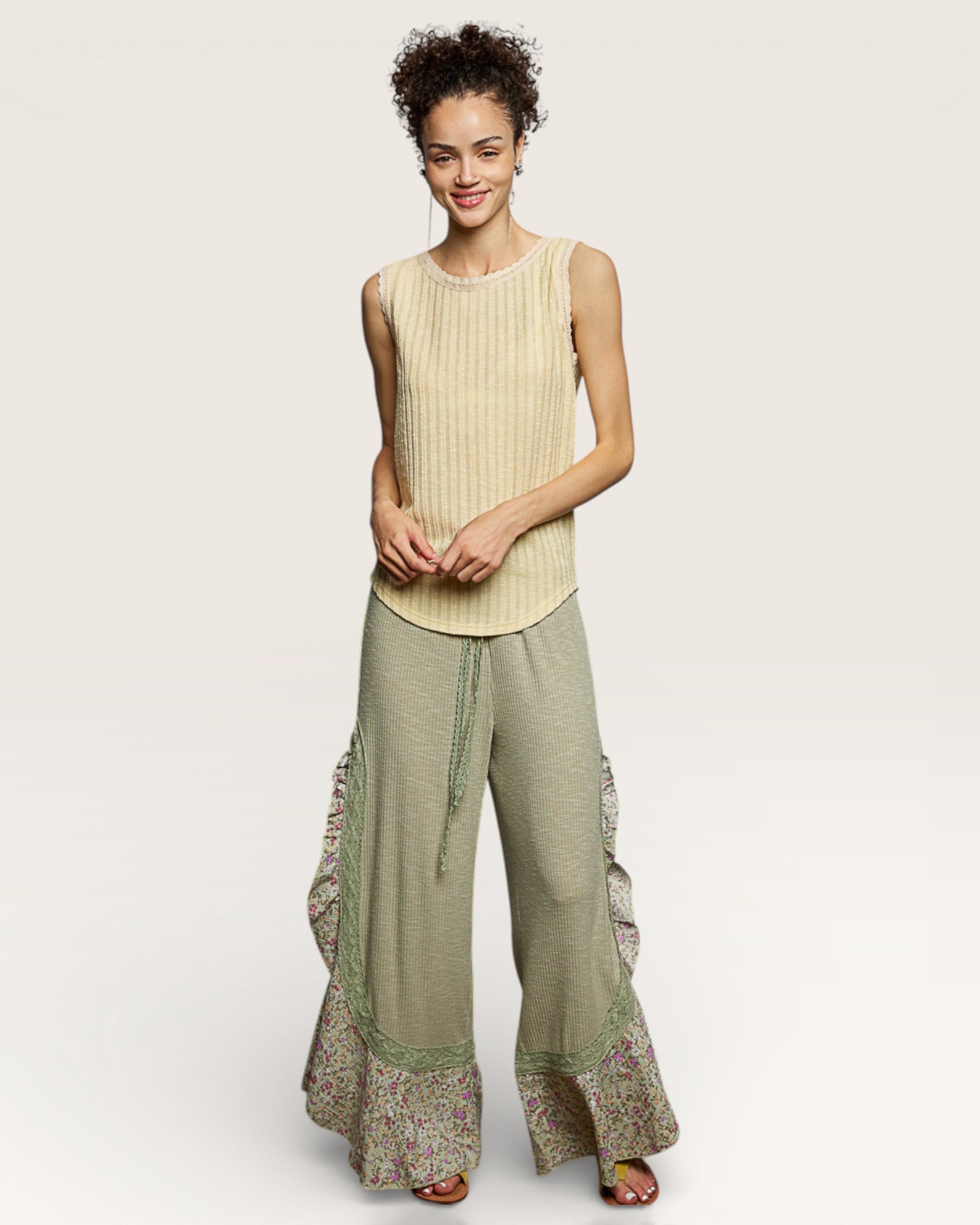 Woman wearing a sleeveless beige top and green patterned pants on a plain background