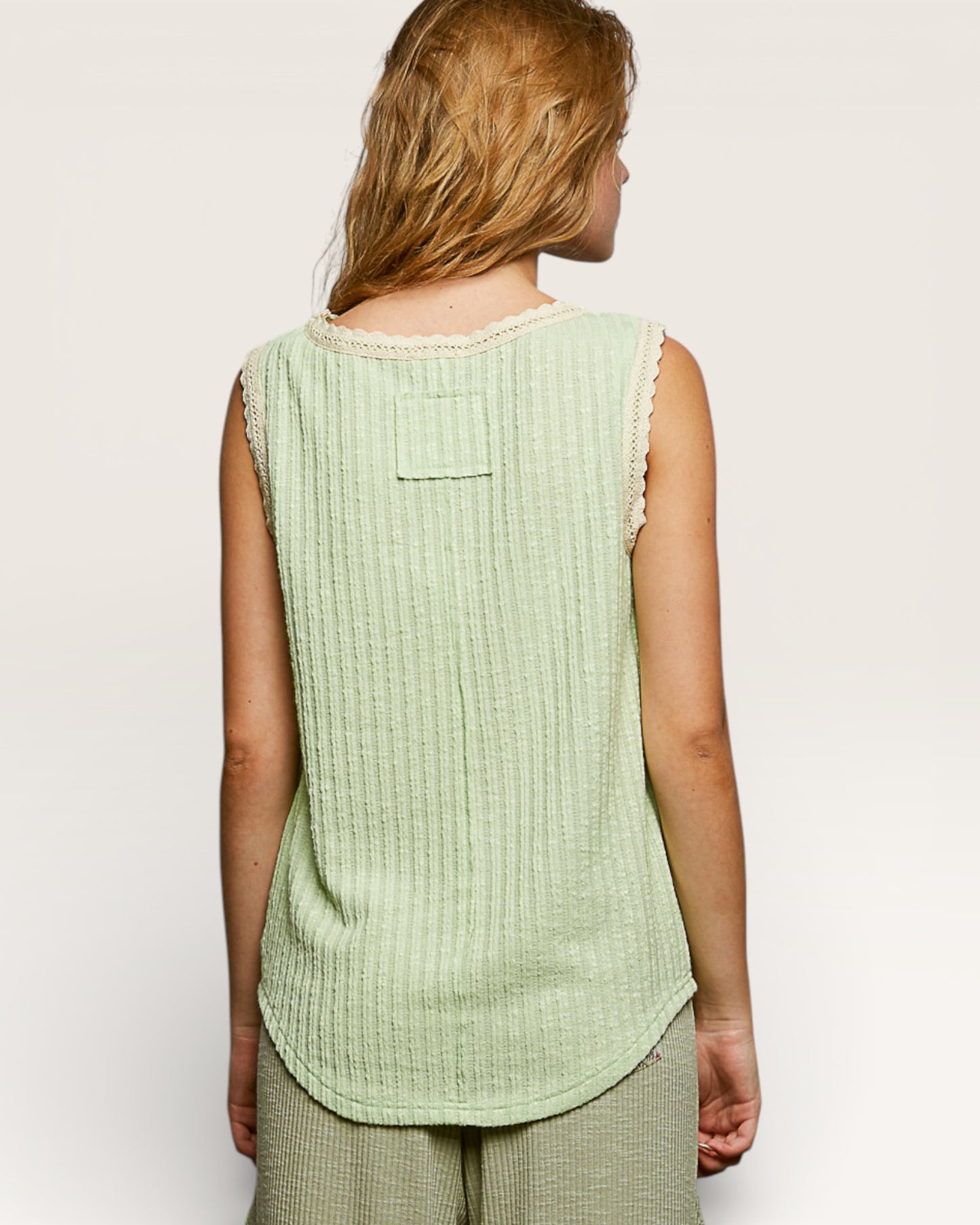 Woman wearing a light green sleeveless top against a plain background