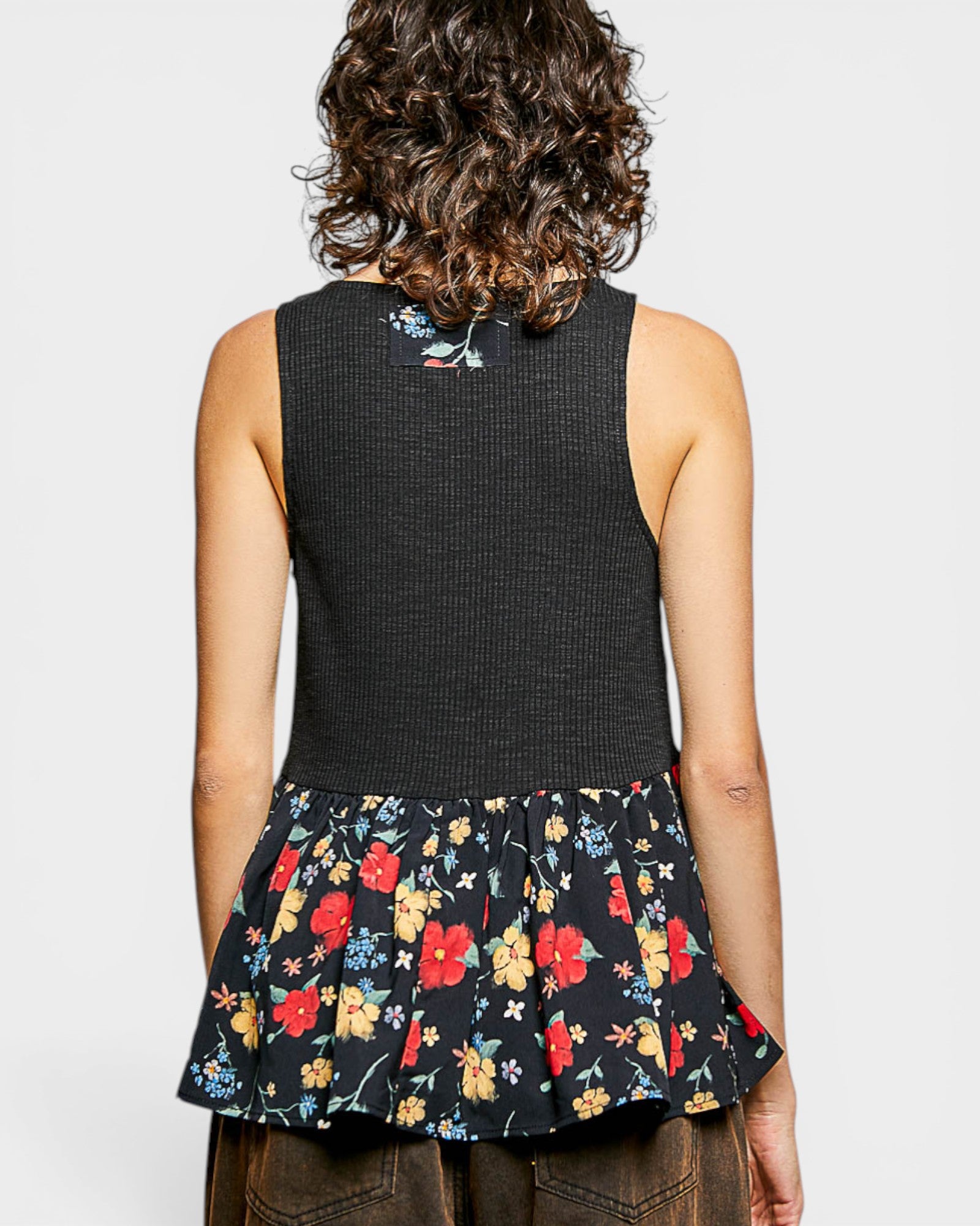Person wearing a black sleeveless top with floral patterned hem on a plain background