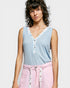 Woman wearing a light blue sleeveless top with floral details and pink pants on a plain background
