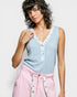 Woman wearing a light blue sleeveless top with floral trim and pink pants against a white background