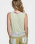 Person wearing a sleeveless green top with floral pattern on the neckline, beige pants with white embroidery, and a belt.