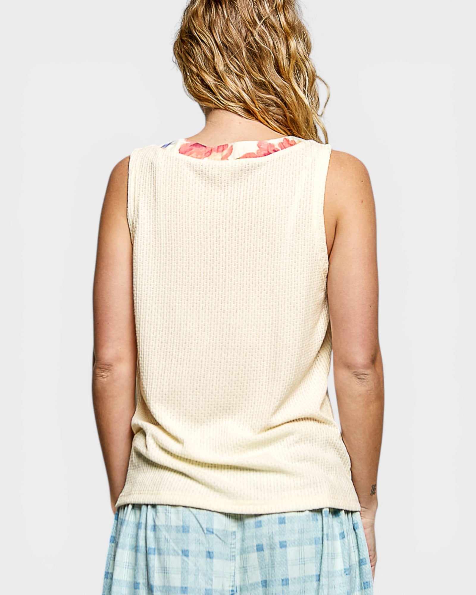 Person wearing a beige sleeveless top with floral pattern on a plain background