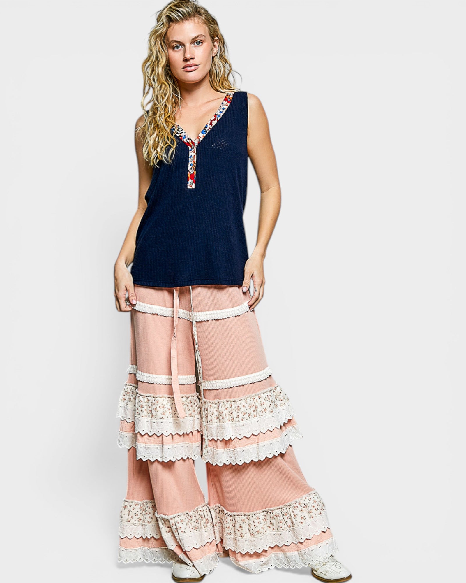 Woman wearing a navy sleeveless top with floral embroidery and pink lace-trimmed pants on a white background