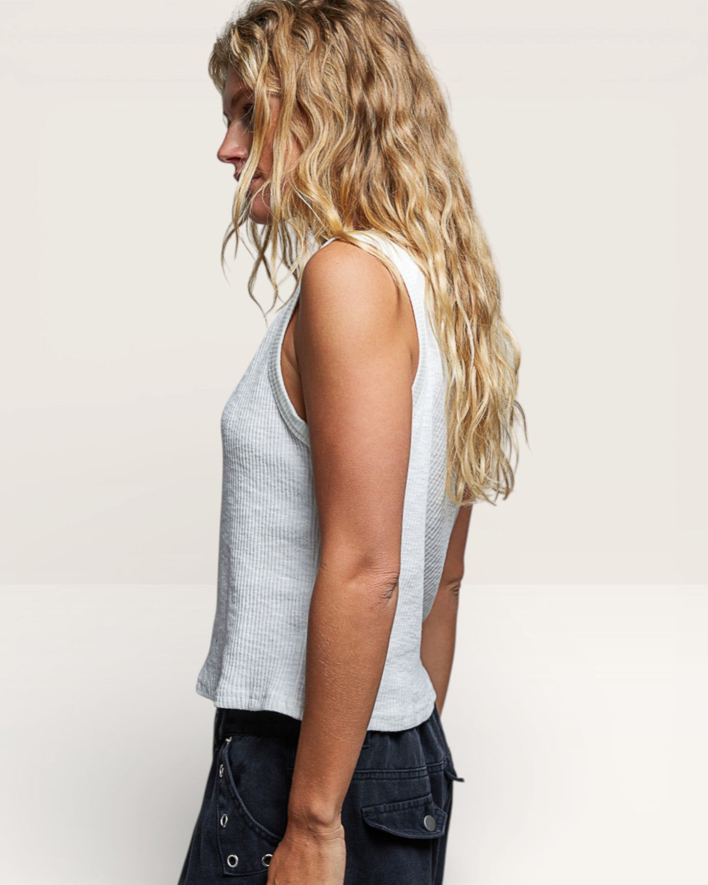 Woman wearing a sleeveless top and dark pants on a plain background