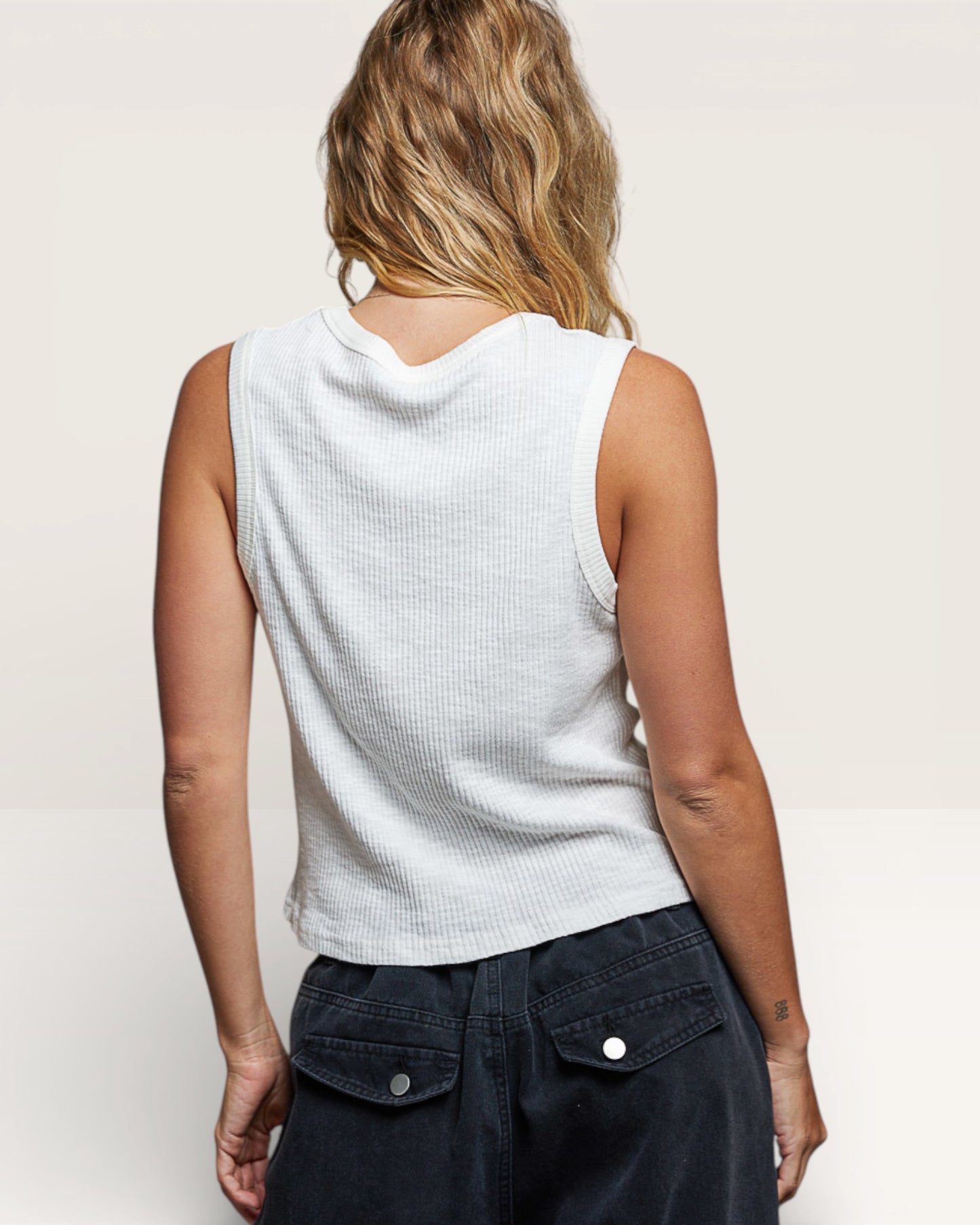 Person wearing a white sleeveless top and dark pants on a plain background