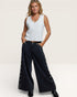 Woman wearing a white sleeveless top and black pants with decorative elements on a plain background