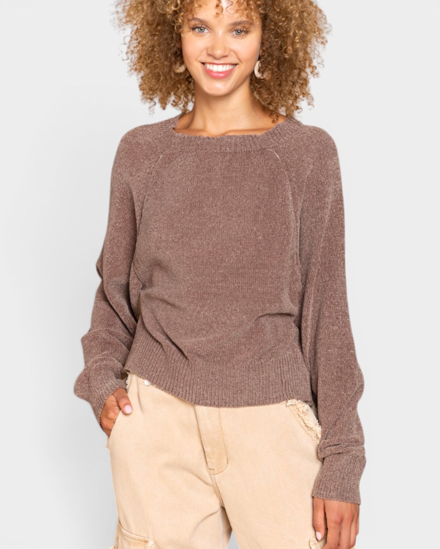 Woman wearing a brown sweater and beige pants against a white background