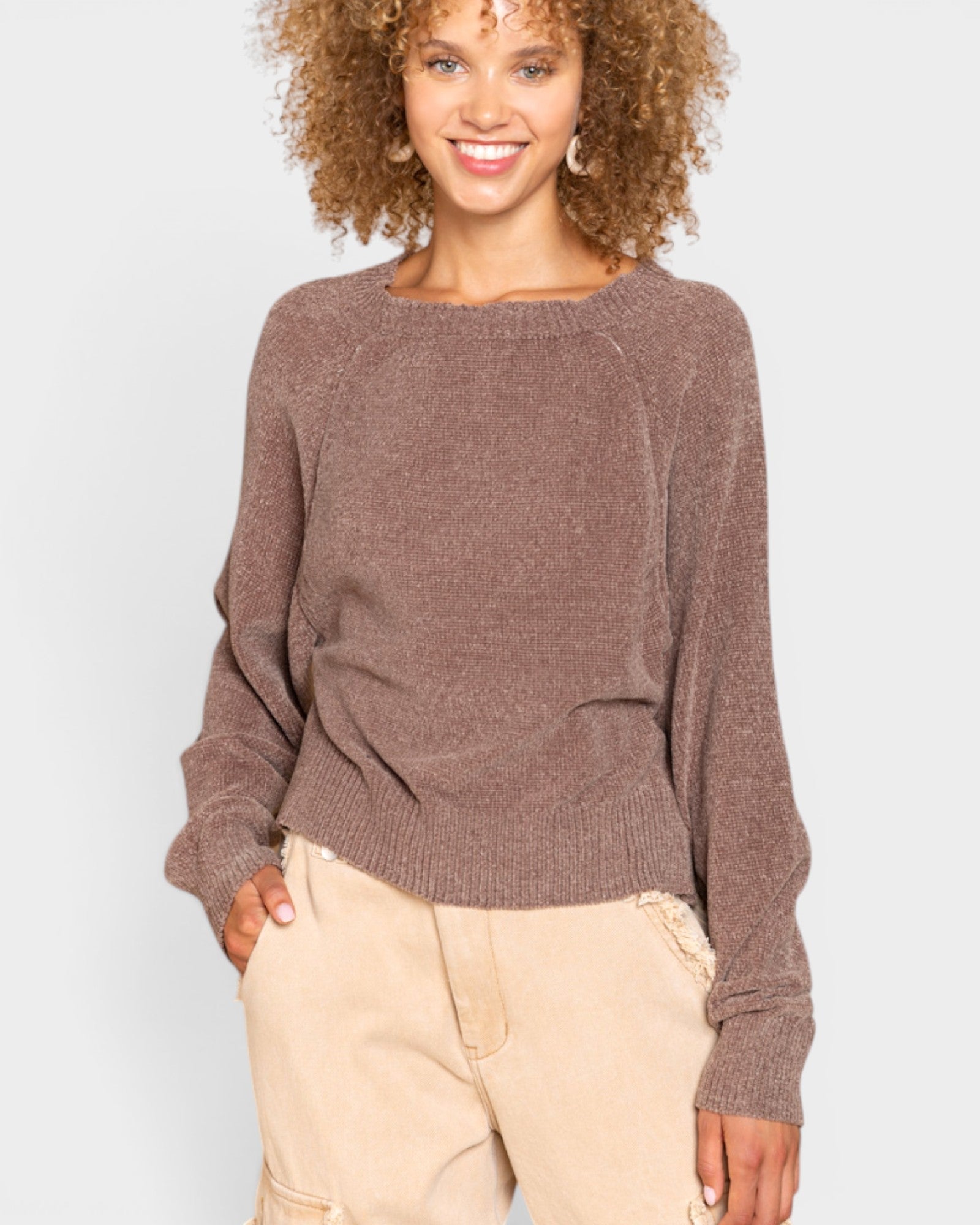 Woman wearing a brown sweater and beige pants against a white background
