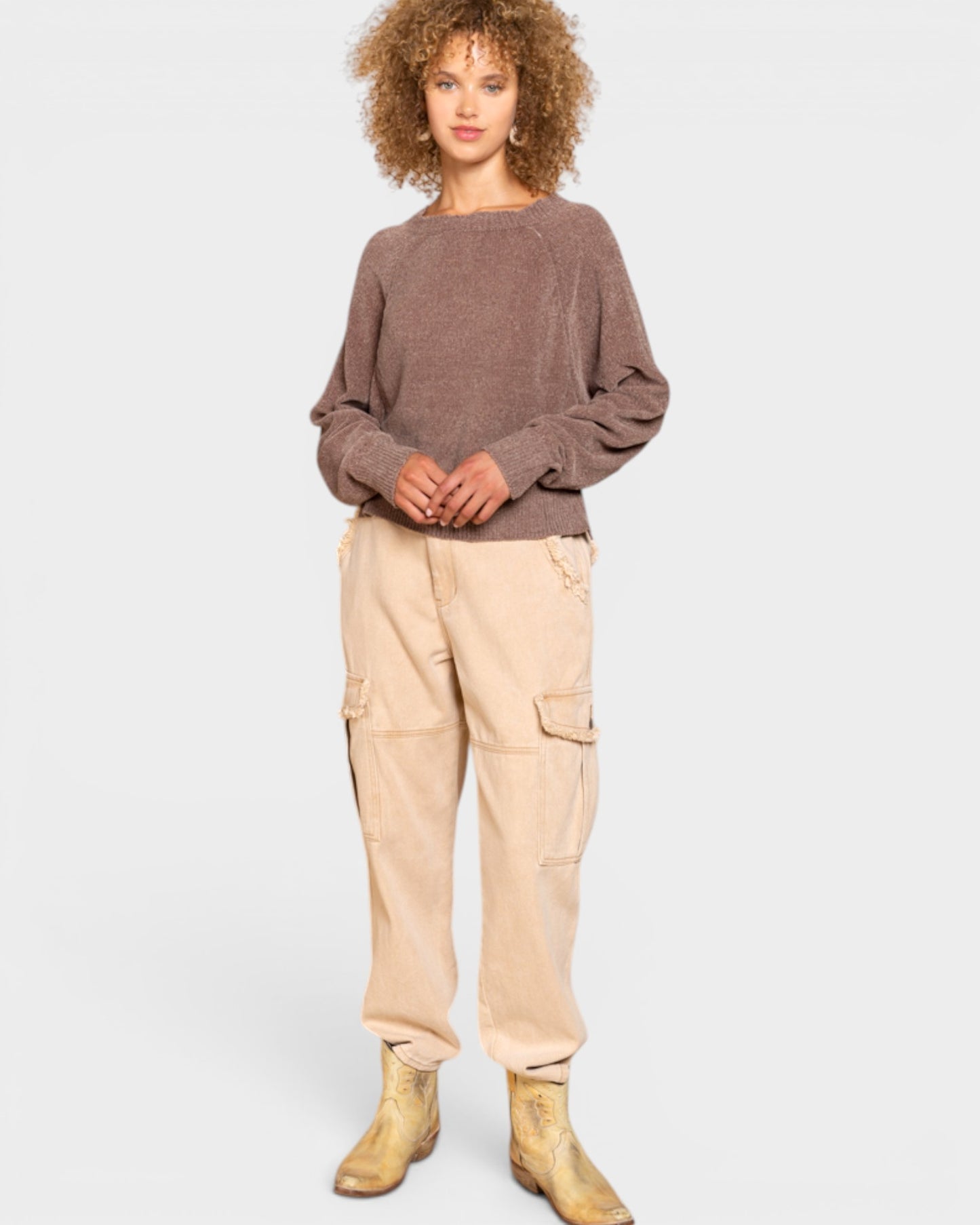 Person wearing a brown sweater and beige cargo pants on a white background
