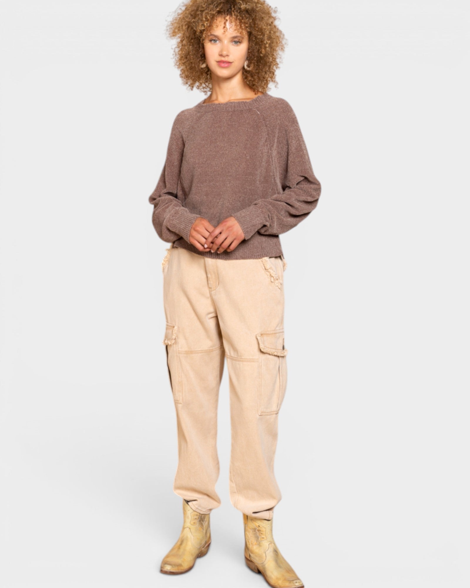 Person wearing a brown sweater and beige cargo pants on a white background