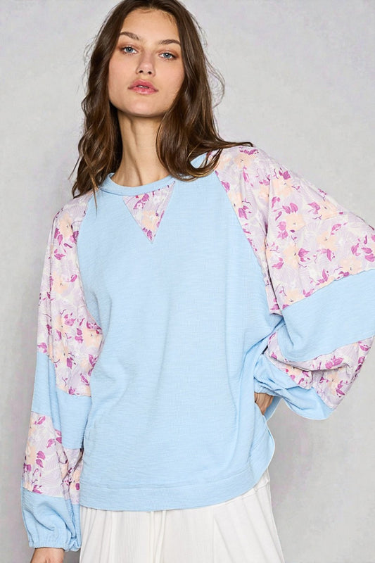 Woman wearing a light blue sweatshirt with floral sleeves against a gray background