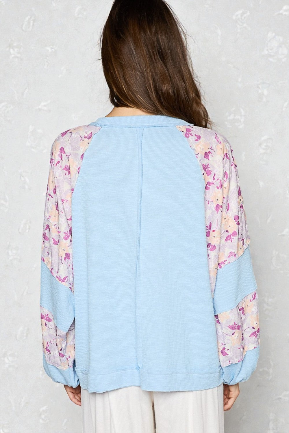 Light blue top with floral sleeves worn by a person against a white background