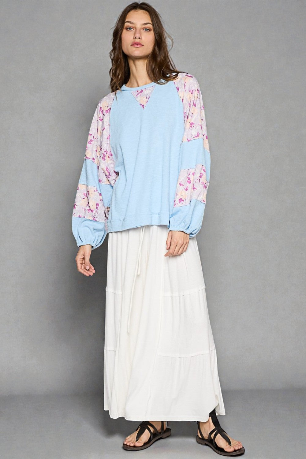 Woman wearing a light blue floral blouse and white skirt against a gray background