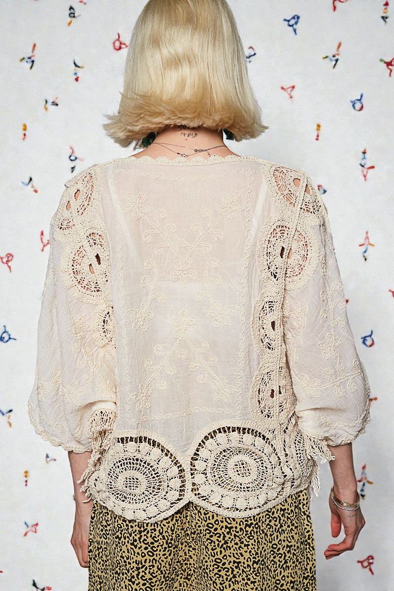 Person wearing a beige embroidered blouse with a colorful patterned background