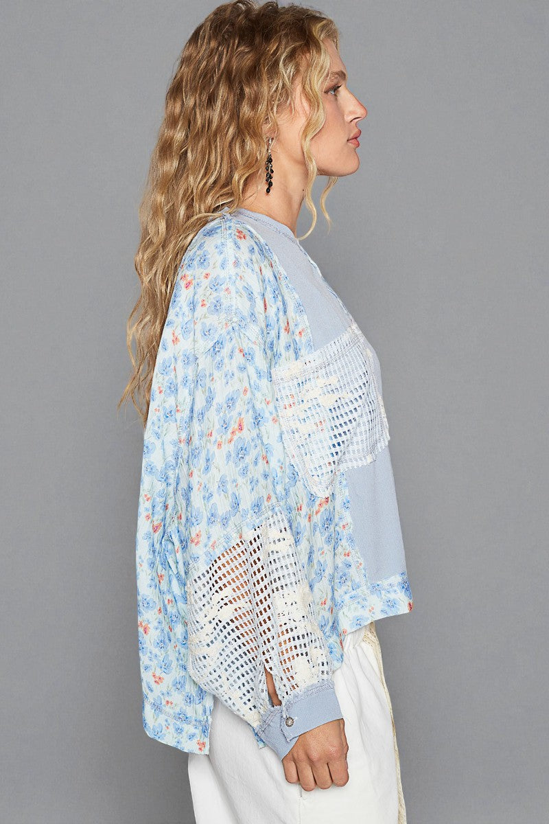 Woman wearing a light blue floral blouse with a sheer overlay against a gray background