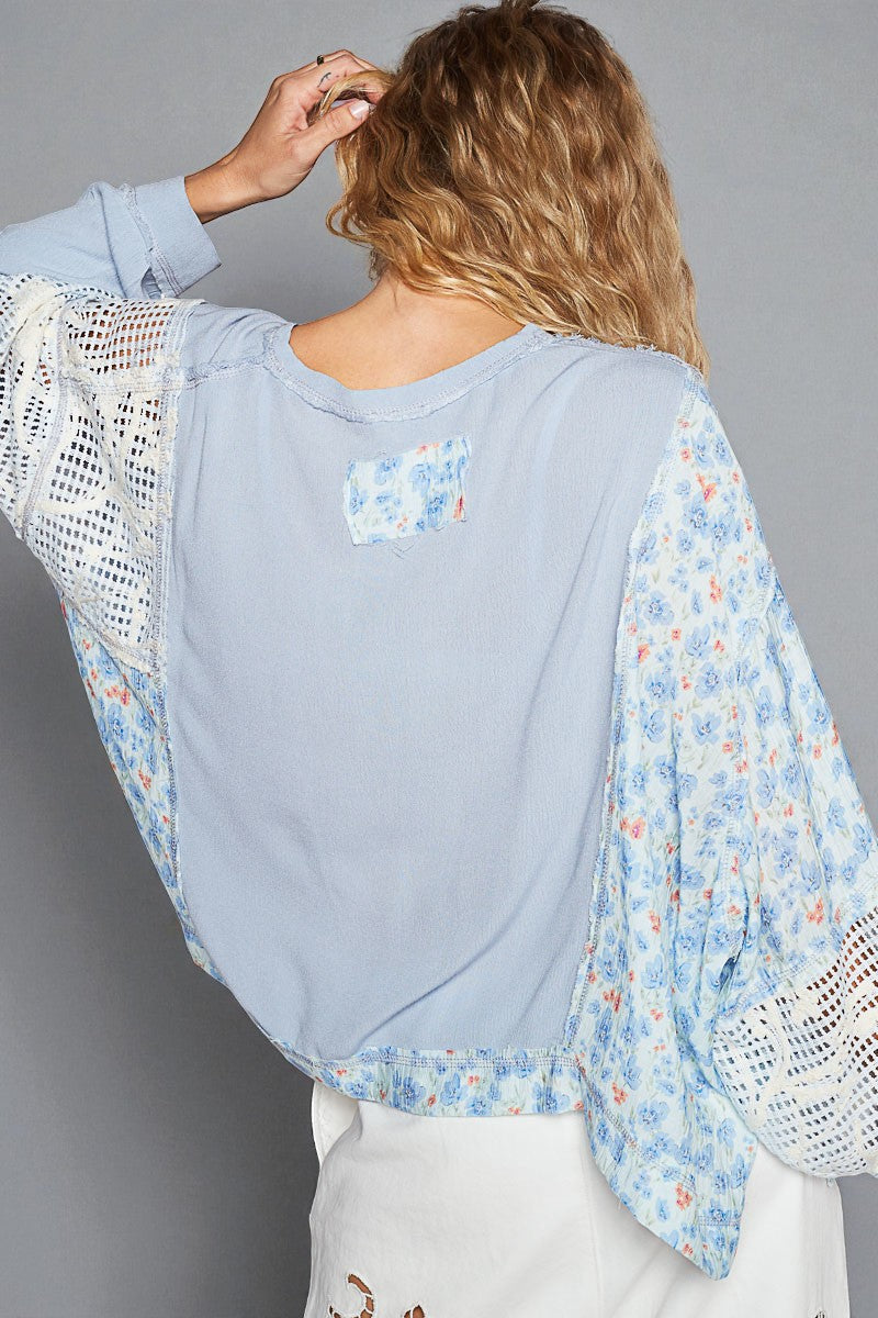 Woman wearing a light blue floral kimono-style top with white sleeves against a gray background