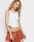 Woman wearing a white sleeveless top with lace details and a rust-colored skirt on a plain background