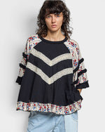 Woman wearing a black sweater with colorful patterns on a plain background