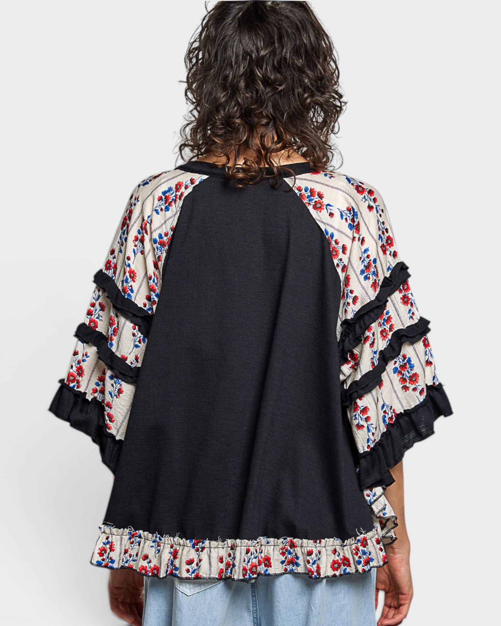 Person wearing a black top with floral sleeves and trim on a white background