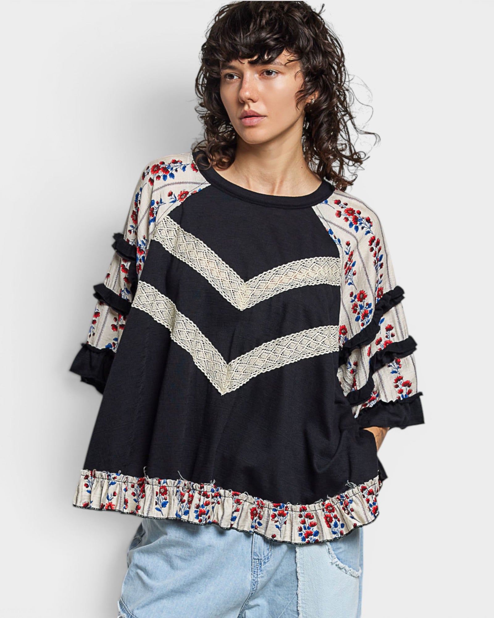 Woman wearing a black sweater with colorful patterns and tassels on a white background